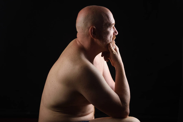 portret van een man shirtloos op zwarte achtergrond, kant kijken - Foto, afbeelding