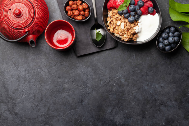 Desayuno saludable con granola casera con yogur y bayas frescas sobre fondo de piedra. Vista superior con espacio de copia - Foto, Imagen