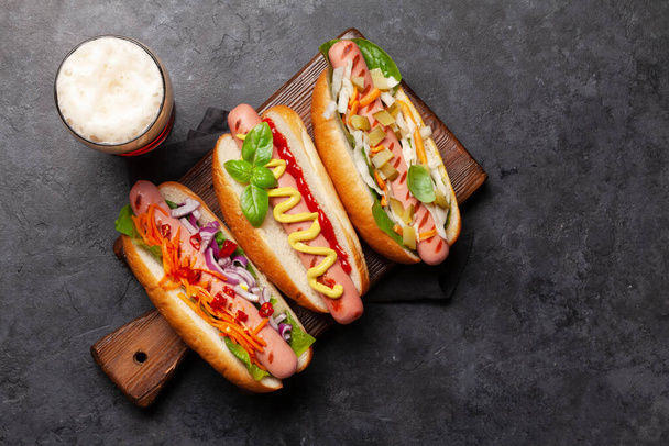 Diverse hotdog met groenten, sla en specerijen en bierglas op stenen ondergrond. Bovenaanzicht met kopieerruimte. Vlakke plaat - Foto, afbeelding