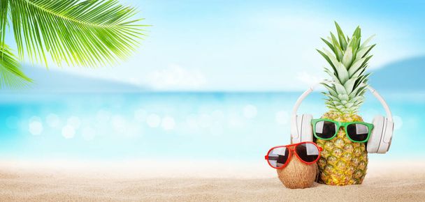 Parlak dalgalı tropikal deniz, güneş gözlüklü ananas ve sıcak kumsalda kulaklık. Kopya alanı ile seyahat ve tatil kavramı - Fotoğraf, Görsel