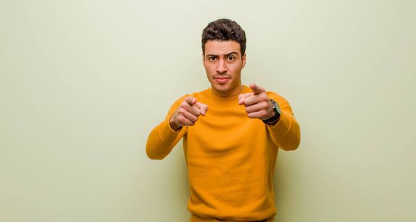 young arabian man pointing forward at camera with both fingers and angry expression, telling you to do your duty against flat wall - Fotoğraf, Görsel