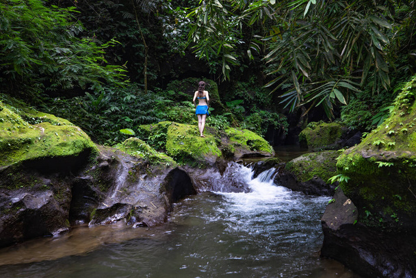 若い旅行者の女性はアジアを探索する。ジャングルや川への眺めをお楽しみください。後ろから見るんだ。青いビキニを着た白人の若い女性。旅行のコンセプト。インドネシアのバリ島バンリ - 写真・画像