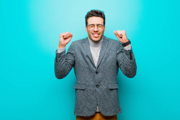 young arabian man looking extremely happy and surprised, celebrating success, shouting and jumping against blue wall - Photo, image