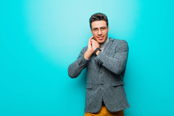 young arabian man feeling in love and looking cute, adorable and happy, smiling romantically with hands next to face against blue wall - Foto, Imagen