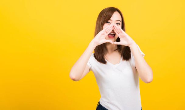 Asian happy portrait beautiful cute young woman teen standing big shout out with hands next mouth giving excited positive looking to camera isolated, studio shot on yellow background with copy space - Foto, imagen