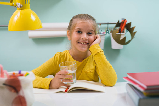 front view of girl sitting table at her room and holding glass of water - Fotoğraf, Görsel