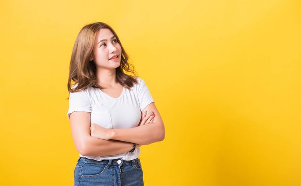 Asian Thai happy portrait beautiful cute young woman standing wear t-shirt her smile confidence with crossed arms looking to side up isolated, studio shot on yellow background and copy space - Фото, изображение