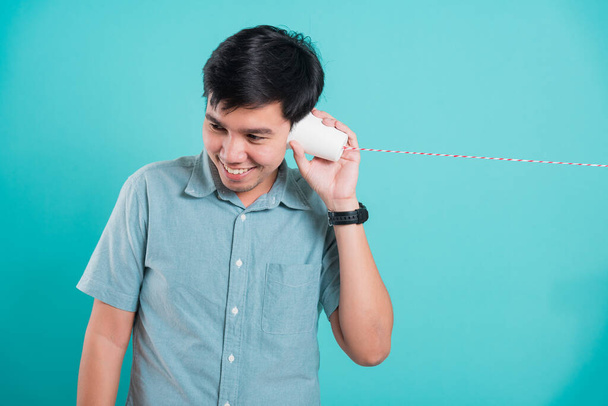 Portrait happy Asian handsome young man smile white teeth standing wear shirt, He holding paper can telephone for listening the message, studio shot on blue background - Fotoğraf, Görsel