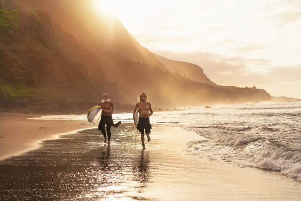 Szczęśliwi surferzy biegający po plaży z deskami surfingowymi - Sportowi przyjaciele surfujący i trenujący na wakacjach na tropikalnym wybrzeżu - Ludzie ekstremalny styl życia sportowego - Zdjęcie, obraz
