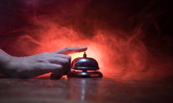 Calling service bell on wooden table with toned lights on dark background. Hotel reception bell, Hand ringing in service bell , selective focus - Photo, Image