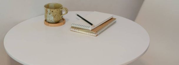 Oříznutý záběr čtecího koutku s šálkem, diáři a kopírovacím prostorem na bílém konferenčním stolku  - Fotografie, Obrázek