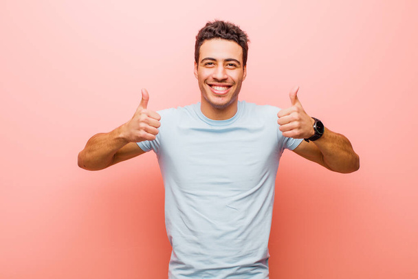 young arabian man smiling broadly looking happy, positive, confident and successful, with both thumbs up against pink wall - Zdjęcie, obraz