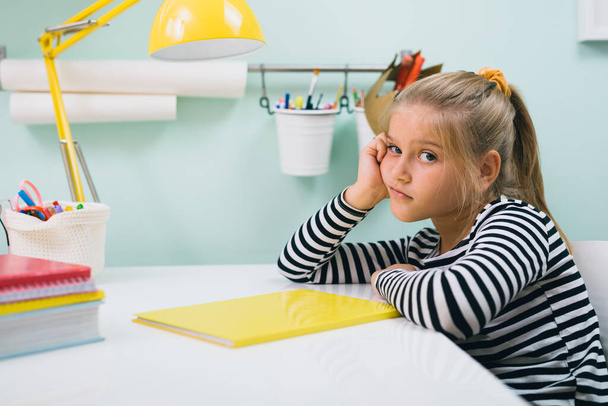 söpö pieni tylsistynyt koulutyttö istuu pöydän hänen huoneessaan - Valokuva, kuva