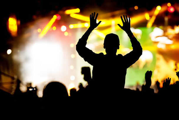 Silueta de hombre con las manos en alto en concierto. Multitud en el espectáculo de música
 - Foto, imagen