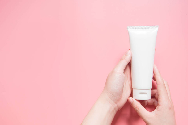 Young female hands holding blank white squeeze bottle plastic tube on pink background. Packaging of cream, lotion, gel, facial foam or skincare. Cosmetic beauty product branding mock-up. Copy space. - Fotoğraf, Görsel