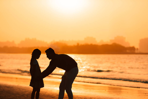 Silueta de niña y papá en la puesta de sol en la playa
 - Foto, Imagen