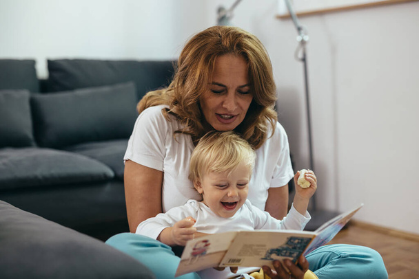 grandmother with her grandson reading picture book together at home - Foto, imagen
