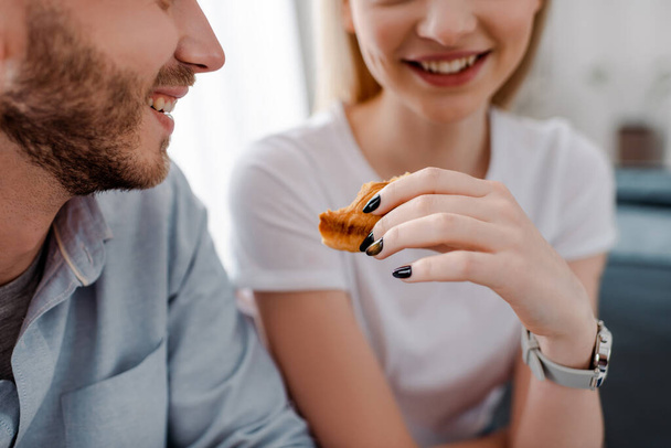 cropped view of happy girl holding croissant near cheerful boyfriend  - Foto, Bild
