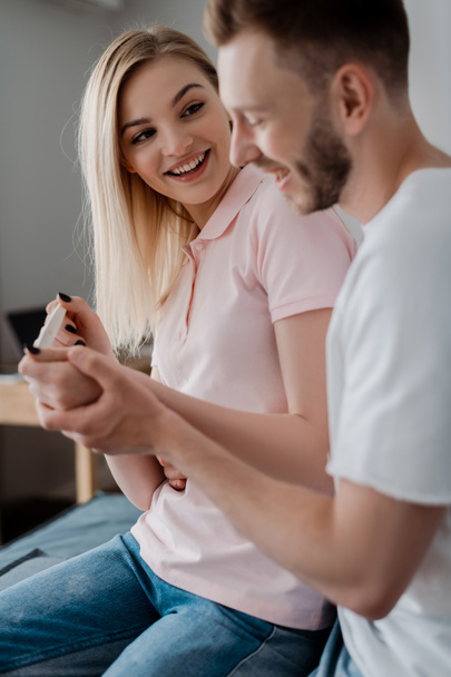 selective focus of happy girl holding pregnancy test with positive result near cheerful boyfriend  - Fotografie, Obrázek