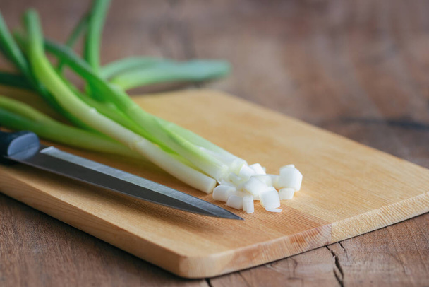 Fresh spring onion and kitchen knife put on wood cutting board on wood table with copy space. Prepare scallions for homemade cooking. Food and vegetable concept for background or wallpaper. - Photo, Image