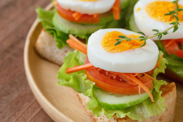Open faced sandwich with toast lettuce tomato carrot cucumber and boil egg on wooden plate in close up view. Delicious breakfast for family served on wood table. Homemade and healthy food concept. - Photo, Image