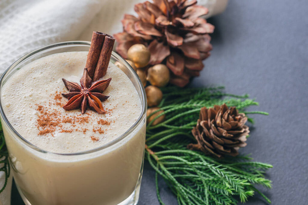 Eggnog, traditional drink for Christmas celebration party in glass topped with ground nutmeg and cinnamon stick, close up in top view with copy space. Concept to present Xmas delicious beverage. - Foto, Imagem
