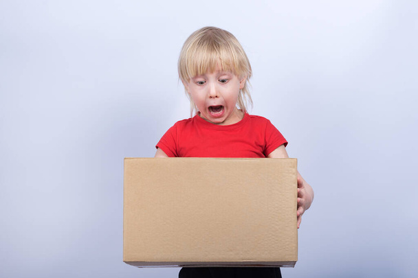 Child holds in hands big box and stares at it. Boy holding box on white background - Foto, immagini