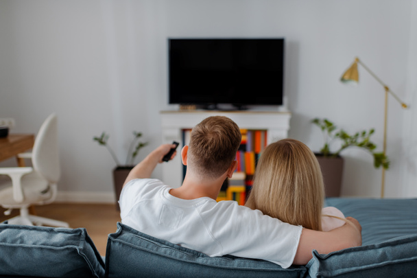vista trasera del hombre y la mujer sentados cerca de la televisión de panel plano con pantalla en blanco
 - Foto, imagen