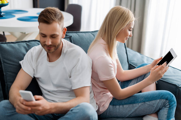 valikoiva painopiste mies käyttää älypuhelinta lähellä nainen tilalla digitaalinen tabletti tyhjällä näytöllä  - Valokuva, kuva