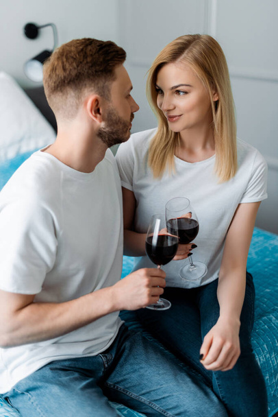 счастливые мужчина и женщина держа очки с красным вином и глядя друг на друга
 - Фото, изображение