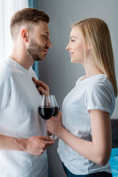 πλαϊνή άποψη του ευτυχισμένος άνθρωπος και γυναίκα κρατώντας ποτήρια με κόκκινο κρασί  - Φωτογραφία, εικόνα