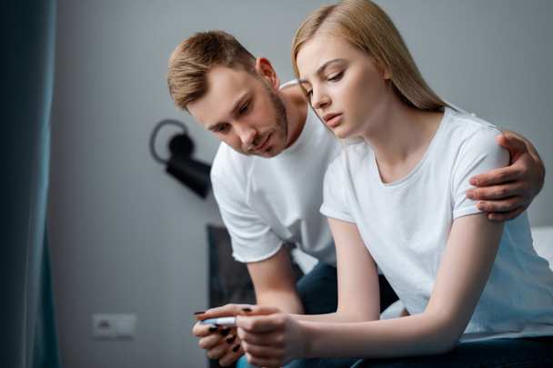 sad man and frustrated girlfriend looking at pregnancy test at home - Foto, Bild
