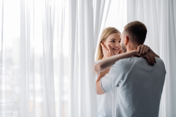 gelukkig vrouw glimlachen terwijl knuffelen man thuis  - Foto, afbeelding