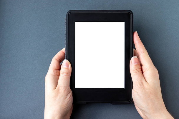 A modern black electronic book with a white blank empty screen in female hands on a gray paper background. Mockup tablet closeup - Photo, Image
