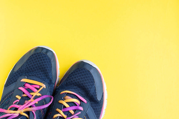 Donkerblauwe sneakers met veelkleurige roze, paarse, gele veters op een felgele achtergrond met kopieerruimte. Concept sport, fitness, workout, hardlopen - Foto, afbeelding