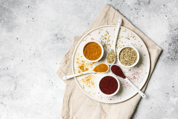 Spices and condiments in white bowls on a light gray table. Turmeric, ginger, curry, fennel and sumac in white bowls. Spices close up - Photo, Image