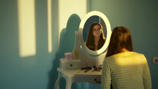 Nettes brünettes Mädchen mit Brille schaut ihr Spiegelbild im Spiegel an - Filmmaterial, Video