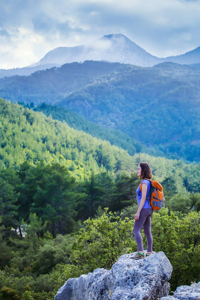 Жінка з рюкзаком стоїть на вершині гори і захоплюється красою гірської долини, дівчина подорожує в красиві місця, досягаючи мети. Красивий пейзаж
. - Фото, зображення