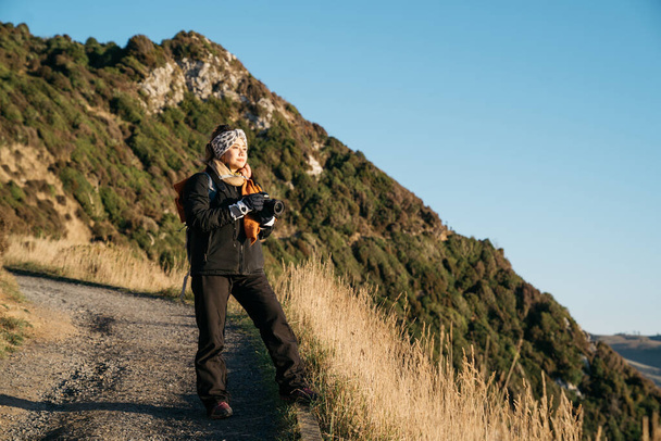 Belo turista asiático tirar alguma foto em Nugget Point, Dunedin, Nova Zelândia. Jovem asiático viajante gosta de caminhar de manhã ao longo da costa da Nova Zelândia. Imagem de estilo de vida com paisagem natural
. - Foto, Imagem