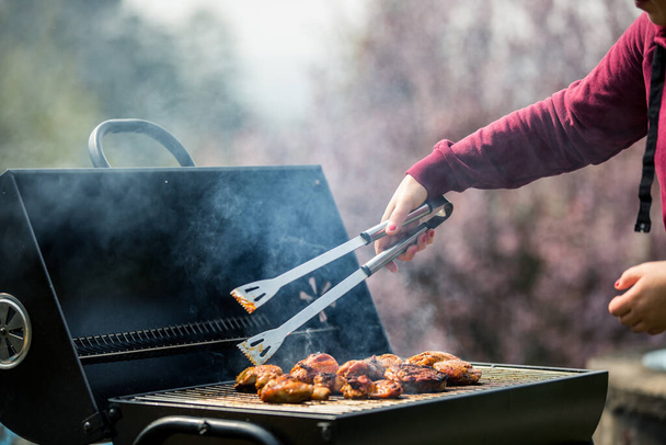 Młoda kobieta grilluje jakiś rodzaj marynowanego mięsa i warzyw na grillu gazowym w okresie letnim, grill - Zdjęcie, obraz