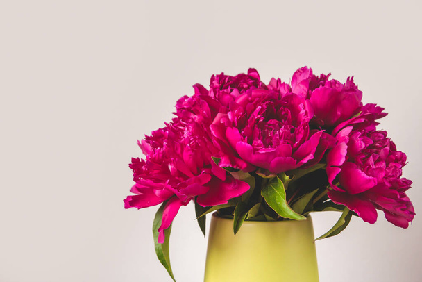 A bouquet of bright pink peonies in a green vase copy space. Blooming peonies. A bouquet of peonies as a gift. - Zdjęcie, obraz