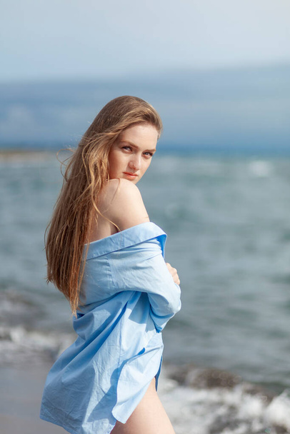 Beautiful young blonde girl in a blue shirt relaxing on the sea, resort - Photo, image