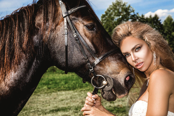 Egy sötét ló és egy nő portréja. Gyönyörű elbűvölő nő egy lóval. Portré egy szépség szőke menyasszony esküvői ruha lóval. - Fotó, kép