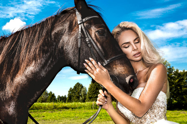 暗い馬と女性の肖像画。馬と美しい魅力的な女性。馬と結婚式のドレスで美しいブロンドの花嫁の肖像. - 写真・画像