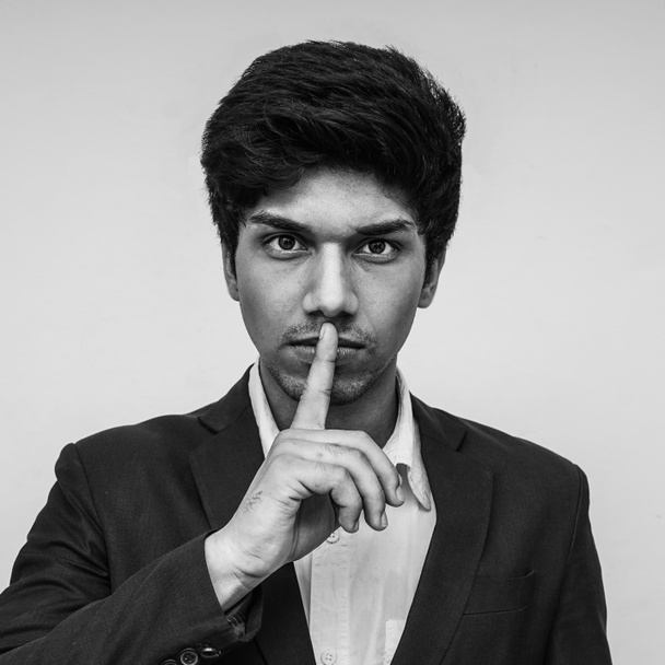 close up studio portrait of young boy with finger on his lips in silence and shut up hand gesture warning or threatening not to speak in political censorship and coerced freedom of speech - Photo, Image
