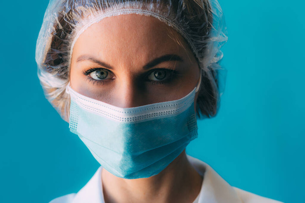 Close-up portrait of young female doctor in medical cap and white gown on blue background with space for text. Female doctor in clinic, tired doctor after hard day on period coronavirus epidemic - Valokuva, kuva