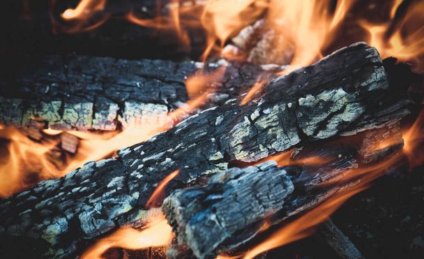 Fascynujące ognisko, świecące drewno i wijące się płomienie. Tekstura płonącego drzewa. Ognisko na charakter do gotowania. - Zdjęcie, obraz