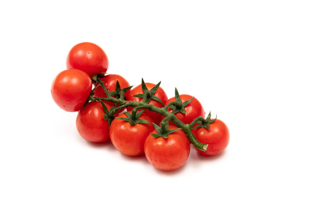 Una rama de tomates rojos cereza sobre un fondo blanco. Las verduras pequeñas y jugosas son ricas en vitaminas y oligoelementos. Comida saludable. Verduras frescas y ecológicas. Alimentos crudos
. - Foto, Imagen