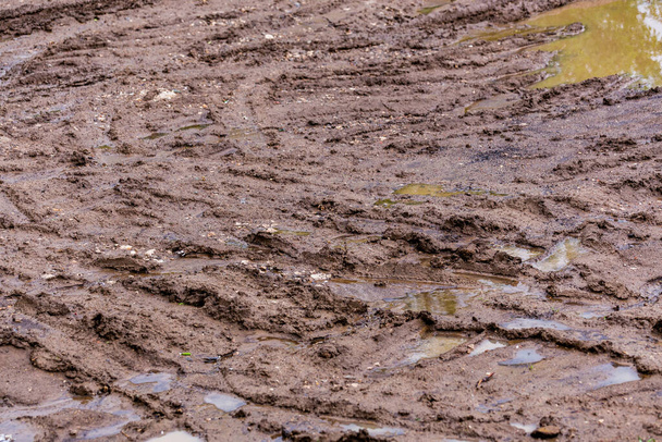 грязная глиняная дорога с лужицами и следами шин - крупный план с избирательным фокусом и размытием
 - Фото, изображение
