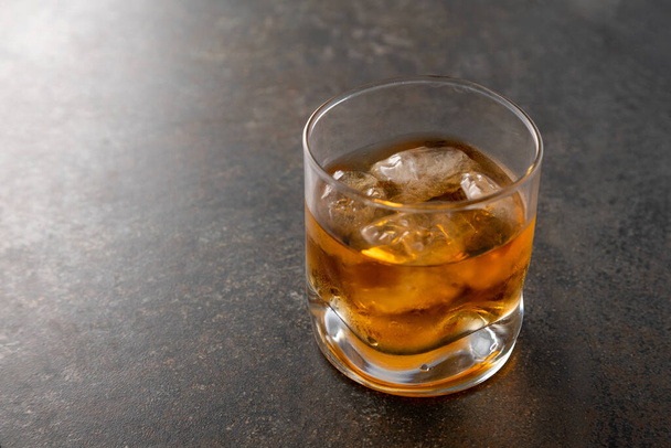 Vaso de whisky dorado envejecido con cubitos de hielo sobre la mesa. Bebida alcohólica de color ámbar con rocas en el bar
 - Foto, Imagen